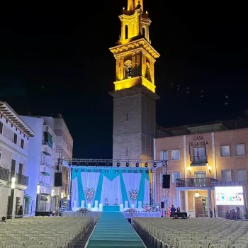 Gran carpa blanca con sillas dispuestas y una torre del reloj al fondo.