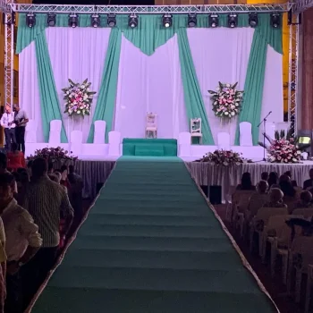 Escenario con cortinas verdes y sillas blancas dispuestas para los invitados.