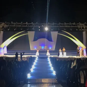 Escenario preparado para una presentación, con luces brillantes y asientos organizados en un ambiente nocturno.