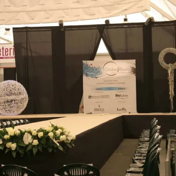 Escenario amplio con rampa, sillas dispuestas y una mesa blanca grande en el centro.