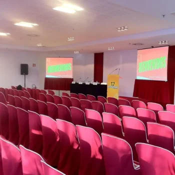 Sala de conferencia con sillas rojas y pantalla de proyector, lista para un evento corporativo.