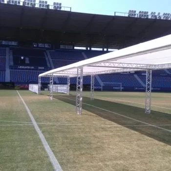 Campo de fútbol con una gran carpa blanca instalada en el centro, rodeada de césped verde.