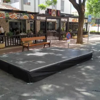 Tarima grande situada al lado de una calle, lista para un evento o presentación pública.