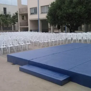 Tarima azul con sillas dispuestas y un tapete azul, lista para un evento o presentación.
