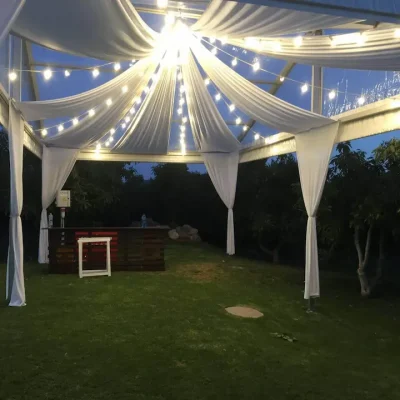 Carpa con cortinas blancas y luces, creando un ambiente elegante y acogedor.