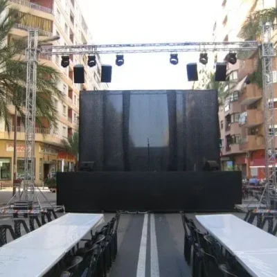 Escenario amplio en una plaza urbana, con luces y decoraciones, listo para un evento.