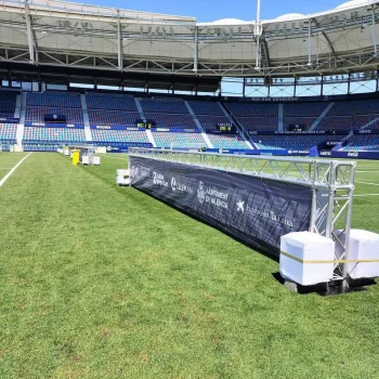 Campo de fútbol con una gran red azul en la portería, rodeado de césped verde y líneas de juego marcadas.