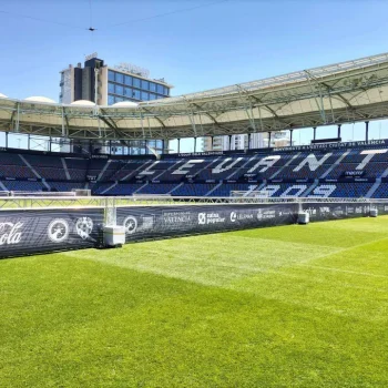 Campo de fútbol con un gran estadio y un letrero visible en la parte superior, rodeado de espectadores.